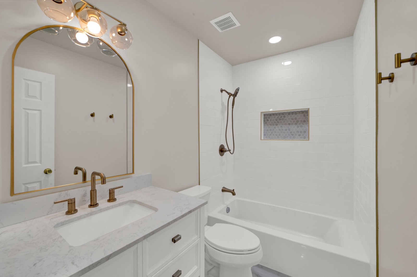 A finished bathroom renovation by Garden State ADU: marble-look vanity, brushed-gold fixtures, subway-tile tub surround with a mosaic accent niche.